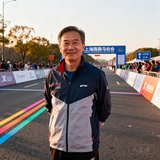 上海路跑协会王会长的户外照片，身穿运动夹克站在马拉松赛道旁